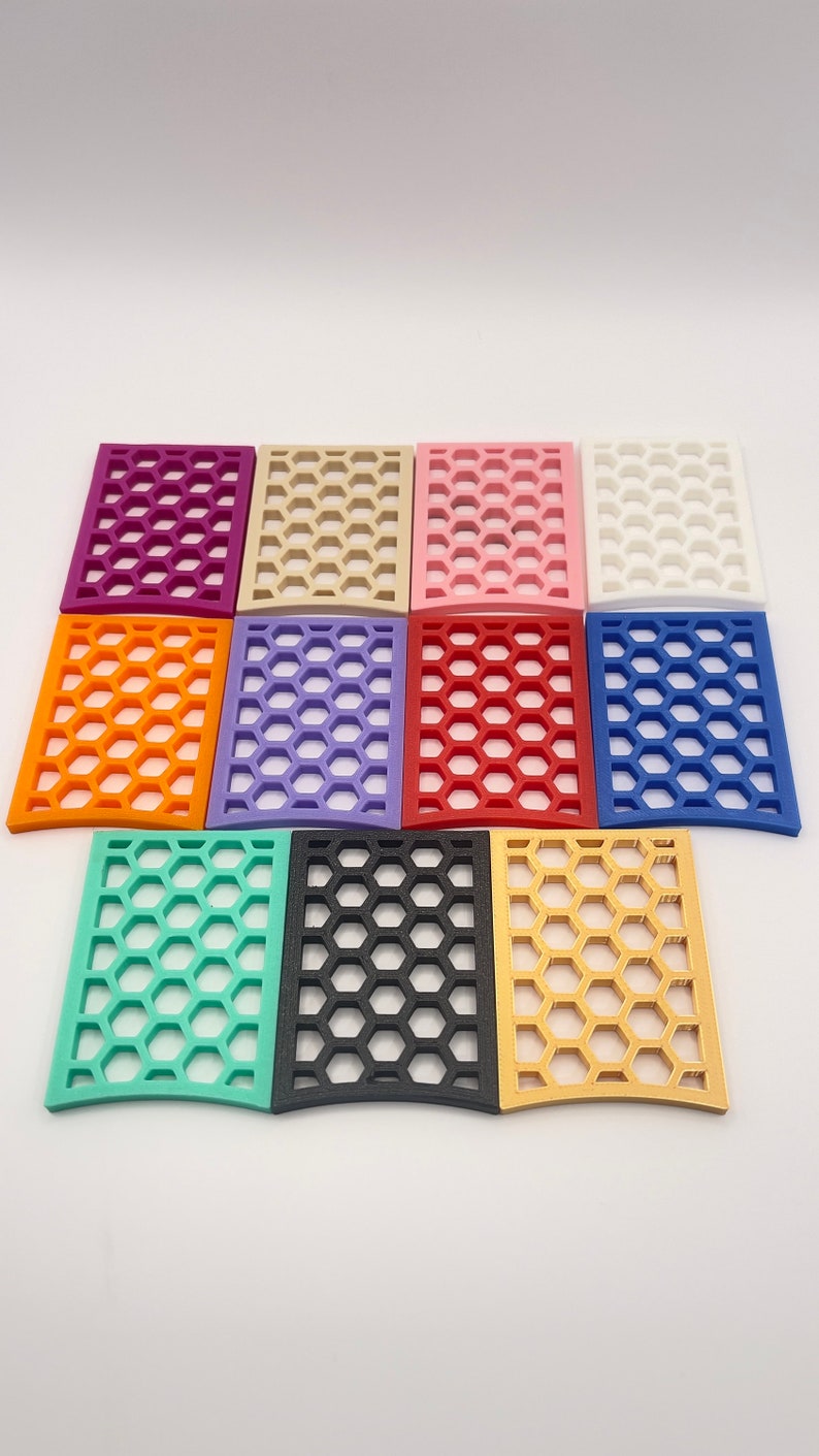 May include: A collection of twelve rectangular decorative panels in various colors, including purple, orange, green, black, and gold. Each panel features a honeycomb pattern, creating a visually appealing design. The panels are arranged on a white surface.