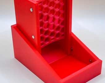 Puede incluir: Una torre de dados roja brillante con una rampa para dados con diseño de panal. La torre es rectangular con una bandeja en la base. La torre es de plástico y tiene un diseño moderno.
