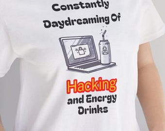 May include: White t-shirt with the text "Constantly Daydreaming Of Hacking and Energy Drinks." The graphic features a laptop and a can of energy drink. The shirt is a casual wear item.