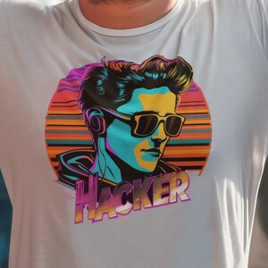 May include: A white t-shirt featuring a retro-style graphic of a person wearing sunglasses and headphones. The graphic is surrounded by a colourful sunset and the word "HACKER" is printed below it.