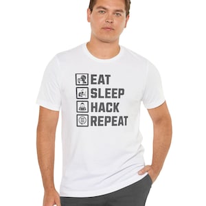 Könnte beinhalten: Weißes T-Shirt mit dem Text "EAT SLEEP HACK REPEAT" in schwarzer, fetter Schrift. Der Text ist in einer vertikalen Liste mit entsprechenden Symbolen angeordnet. Das T-Shirt wird von einer Person getragen.