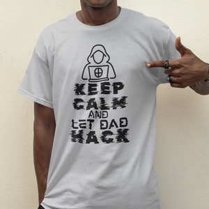 May include: A grey t-shirt with a black graphic of a hooded figure sitting at a computer. The text on the shirt reads "Keep Calm and Let Dad Hack".