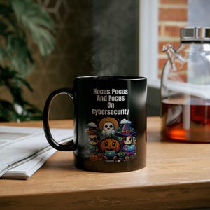 May include: Black coffee mug with a white design featuring a ghost, pumpkin, and witch holding laptops. The text on the mug reads "Hocus Pocus And Focus On Cybersecurity".