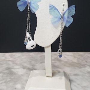 May include: A pair of blue butterfly earrings with a silver chain and a blue crystal charm hanging from each earring.