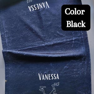 Puede incluir: Una toalla azul oscuro con el nombre "Vanessa" y un contorno blanco de una bicicleta est&aacute;tica. El texto "Color Black" est&aacute; en un cuadro negro en la esquina superior derecha de la toalla.