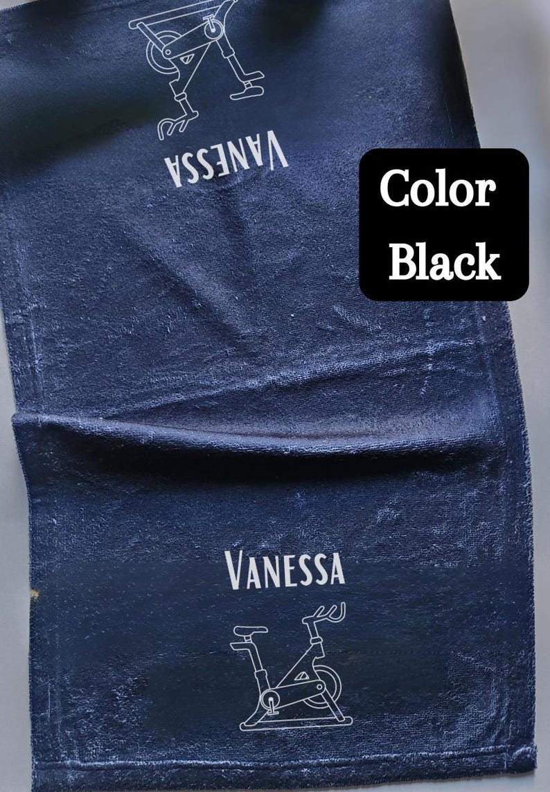 Puede incluir: Una toalla azul oscuro con el nombre "Vanessa" y un contorno blanco de una bicicleta est&aacute;tica. El texto "Color Black" est&aacute; en un cuadro negro en la esquina superior derecha de la toalla.