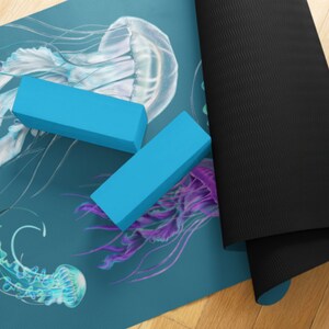 May include: A blue yoga mat with a jellyfish design. The mat is rolled up and has two blue yoga blocks on top of it. The text "The Studio" is visible in the bottom left corner of the mat.