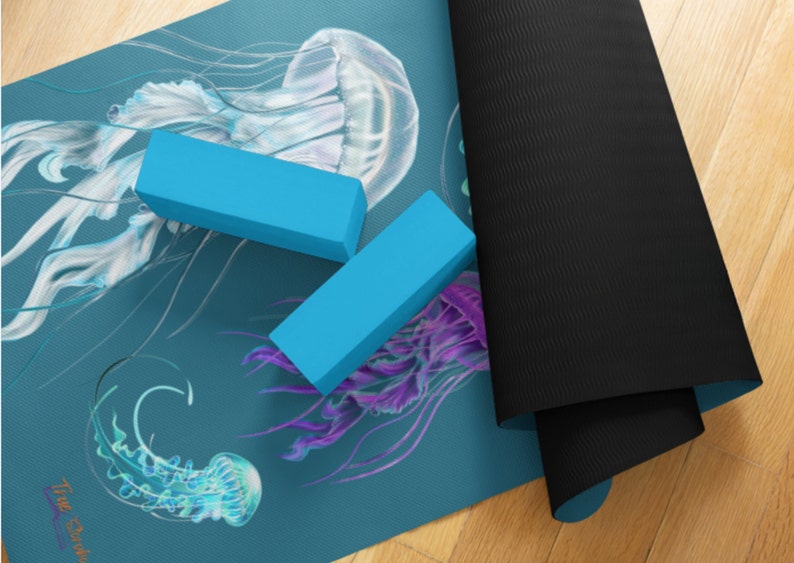 May include: A blue yoga mat with a jellyfish design. The mat is rolled up and has two blue yoga blocks on top of it. The text "The Studio" is visible in the bottom left corner of the mat.