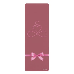 May include: A pink yoga mat with a pink infinity symbol and heart design. The mat has a pink bow on it and the text "The Orchard" at the bottom.