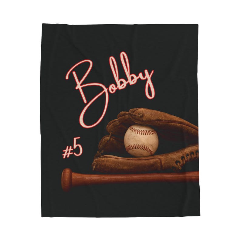 May include: A black and red baseball themed throw blanket with the name "Bobby" written in cursive and the number "#5" in red. A baseball is in a brown leather baseball glove and a brown wooden baseball bat is below the glove.
