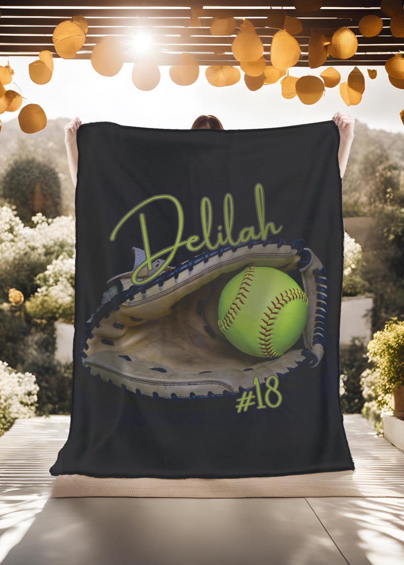 May include: Black fleece blanket with a green softball in a brown catcher's mitt. The text "Delilah #18" is printed in green on the blanket.