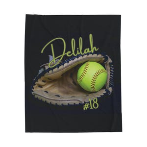 May include: Black and green softball blanket with a yellow softball in a brown catcher's mitt. The text "Delilah #18" is printed on the blanket.