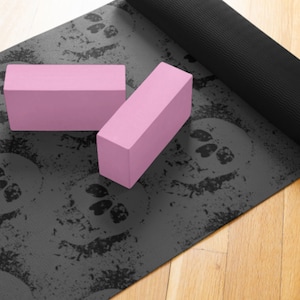May include: A black yoga mat with a skull pattern and two pink yoga blocks. The mat is rolled up and the blocks are lying on top of it.