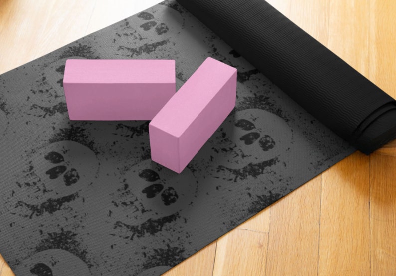 May include: A black yoga mat with a skull pattern and two pink yoga blocks. The mat is rolled up and the blocks are lying on top of it.