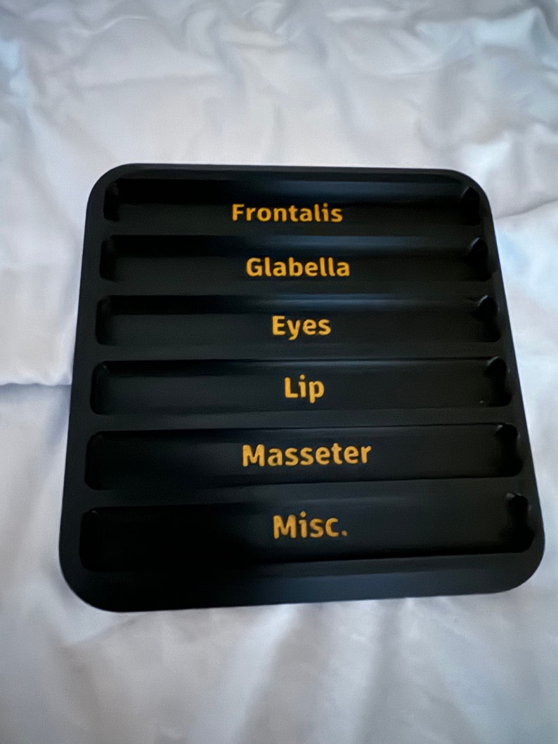May include: Black tray with six compartments labeled "Frontalis", "Glabella", "Eyes", "Lip", "Masseter", and "Misc."