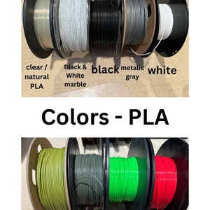 May include: Spools of different colored PLA filament for 3D printing. The colors include clear, black and white marble, black, metallic gray, white, sage green, olive green, neon green, and red.