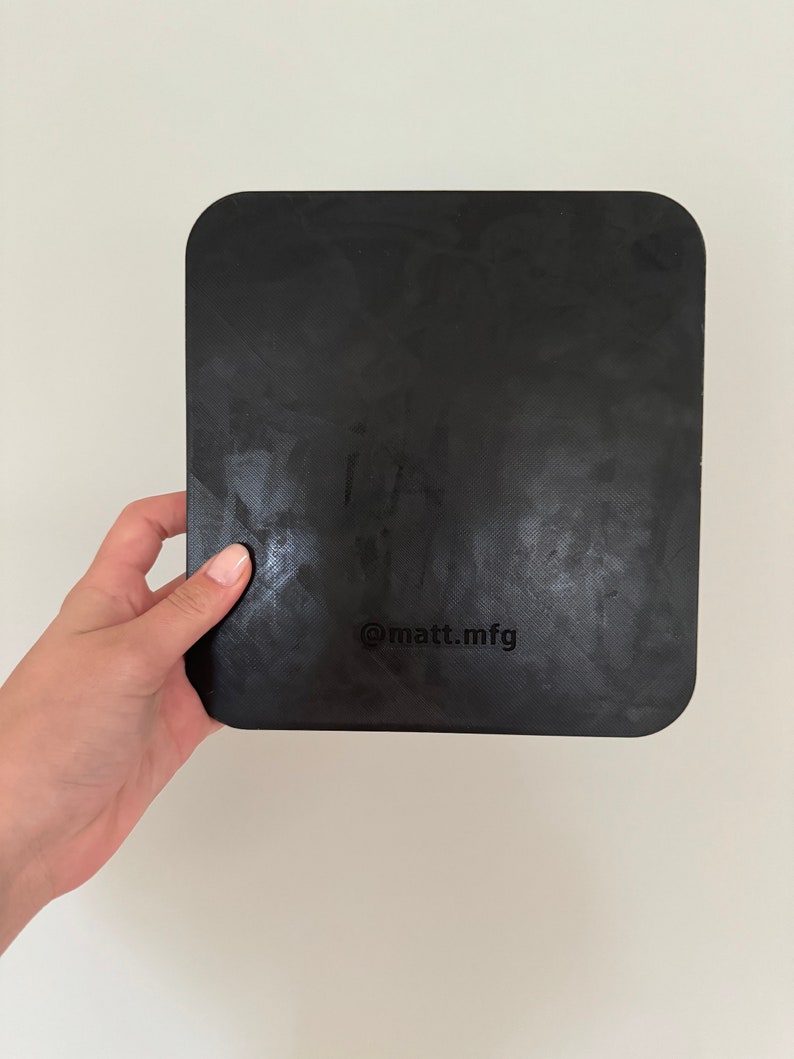 May include: A black square-shaped cutting board with rounded corners. The board has a textured surface and the text "@matt_mfg" is printed on the bottom.
