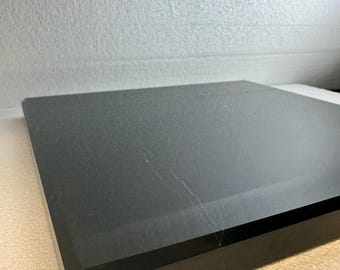 May include: A black, rectangular object with a beveled edge. The surface has a slight sheen and a few visible scratches. The object appears to be made of a solid, dark material.