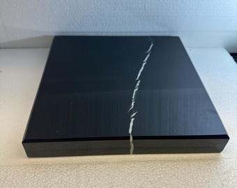 May include: A square, black marble slab with a white vein running diagonally across the surface. The slab has a polished finish and a beveled edge. The marble is set against a neutral background.