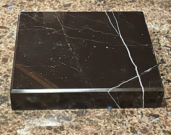 May include: A black marble base with a polished finish. The base has a rectangular shape and a smooth surface.