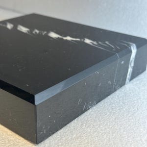 May include: A rectangular black marble box with a white vein running across the top. The box has a polished finish and a clean, modern design. The marble has a natural, textured appearance.