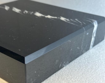 May include: A rectangular black marble box with a white vein running across the top. The box has a polished finish and a clean, modern design. The marble has a natural, textured appearance.