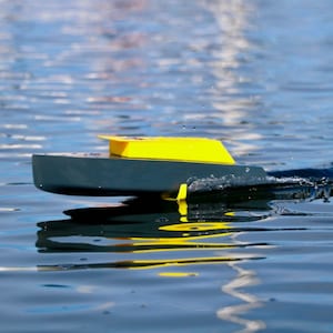May include: A small, black and yellow toy boat with a yellow deck and a black hull, floating on the water.