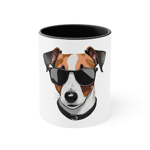 May include: White ceramic mug with a black rim featuring a cartoon illustration of a Jack Russell Terrier wearing sunglasses. The dog has brown and white fur and a black collar.