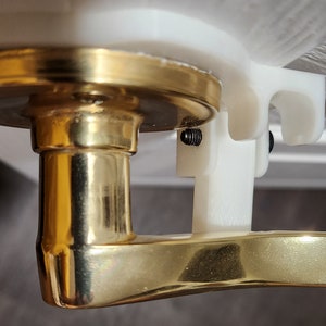 May include: A gold door handle with a white plastic mounting bracket. The handle is attached to the bracket with a screw.