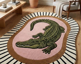 May include: An oval area rug featuring a central green crocodile illustration on a pink background. The rug has a thick brown border surrounded by an outer cream-colored edge with black radial stripes extending toward the perimeter of the rug.