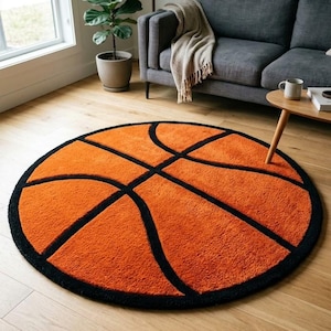 May include: A circular area rug featuring a vibrant orange textured surface with thick black lines arranged in the pattern of a basketball. The rug has a soft, plush pile and a distinct black border that outlines the entire circular shape.