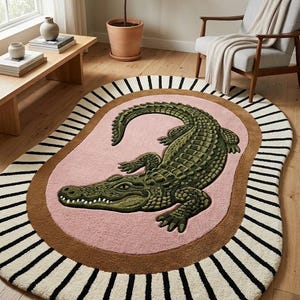 May include: An oval area rug featuring a central green crocodile illustration on a pink background. The rug has a thick brown border surrounded by an outer cream-coloured edge with black radial stripes extending toward the perimeter of the rug.