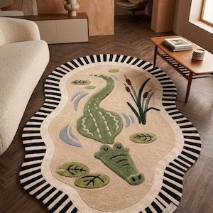 Puede incluir: Una alfombra ovalada con una ilustración central de un cocodrilo verde rodeado de ondas de agua azul claro, nenúfares verdes y espadañas marrones. La alfombra tiene un borde grueso con rayas verticales alternas en blanco y negro.