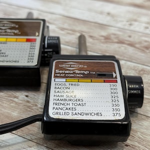May include: A black and brown West Bend Sensa-Temp heat control device with a dial and a list of foods and their corresponding temperatures. The device has a black cord and a black and white knob.