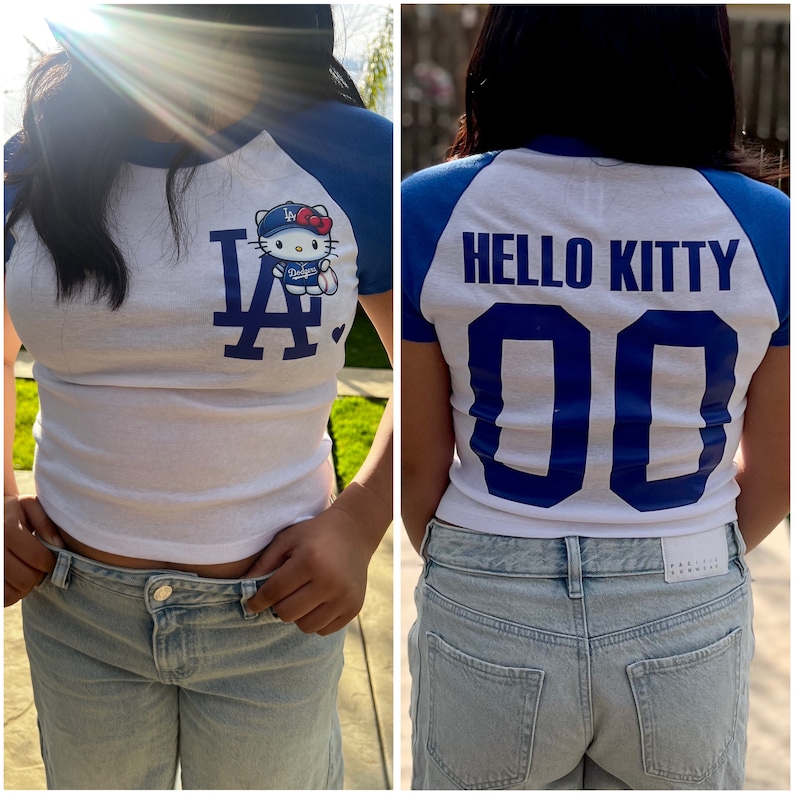 Pu&ograve; includere: T-shirt bianco e blu in stile baseball con il personaggio di Hello Kitty che indossa un berretto da baseball e un'uniforme dei Dodgers. La parte anteriore della maglietta mostra il logo dei Dodgers. La parte posteriore della maglietta dice "HELLO KITTY" e il numero "00".