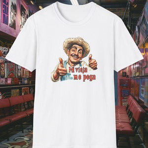 May include: White t-shirt with a cartoon image of a man wearing a straw hat and giving a thumbs up. The text "Mi vieja me pega" is printed on the shirt.