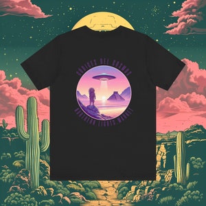 May include: Black t-shirt with a purple circle graphic featuring a person standing in front of a pyramid and a UFO. The text "CODICES DEL COSMOS NORTHERN LIGHTS MARKET" is around the circle.
