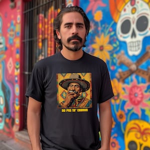 May include: Black t-shirt featuring a colorful illustration of a man wearing a sombrero and smoking a cigarette. The text "NO POS TA' CABRON" is printed below the image. The background is a colorful mural.