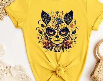 May include: A yellow t-shirt with a black and white sugar skull cat design. The cat is surrounded by colorful flowers and leaves.
