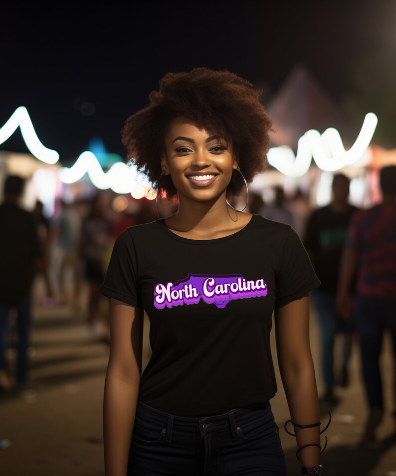 Może przedstawiać: Kobieta w czarnym t-shircie z fioletowym nadrukiem przedstawiającym stan Karolina P&oacute;łnocna i tekstem "North Carolina".