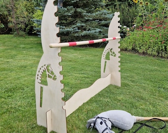 May include: A wooden horse jumping obstacle with a red and white stripe. The obstacle is made of plywood and has a horse head cutout on each side. A gray rocking horse is in the foreground.