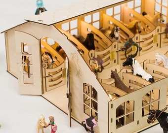 May include: A wooden toy horse stable with multiple stalls, fences, and miniature horses and riders. The stable has a light brown wood finish and a white roof. The miniature horses are brown, black, and white.