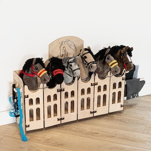 May include: A wooden stable with six horse head stalls, each with a plush horse head inside. The stalls are made of light wood and have a decorative archway at the top. The horse heads are all different colors and have different bridles.