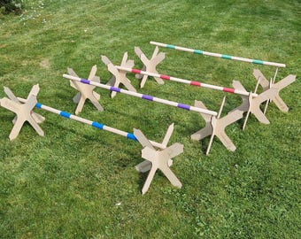 May include: Five wooden jump hurdles with colorful tape on the poles. The hurdles are set up in a row on a grassy surface.