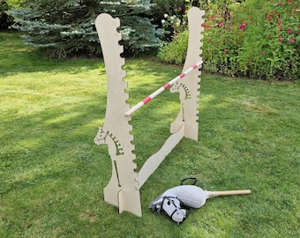 May include: A wooden horse jumping obstacle with a white and red striped bar. A stuffed toy horse with a brown saddle lies on the grass.