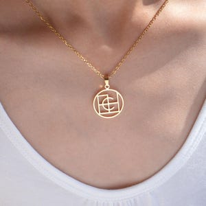Könnte beinhalten: Eine goldfarbene Anhängerkette. Der Anhänger ist ein Kreis mit einem geometrischen Design im Inneren. Die Halskette ist ebenfalls goldfarben und wird um den Hals getragen.