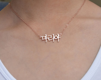 May include: A rose gold-toned necklace featuring a delicate chain and a central pendant displaying the Korean Hangul characters 마리아. The metal has a polished finish, and the pendant is suspended symmetrically from the thin, refined link chain.