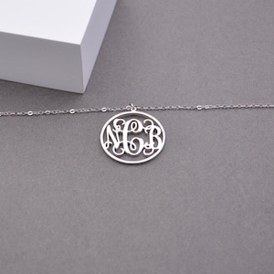 May include: A silver necklace with a circular pendant featuring a monogram of the letters N, C, and B.