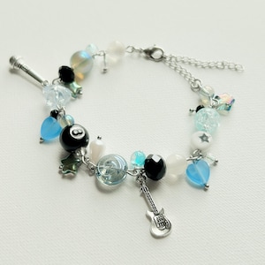 May include: A beaded bracelet with a variety of charms and beads in shades of blue, black, white, and silver. Charms include a microphone, a guitar, and an eight ball. The bracelet is on a white background.