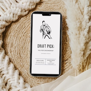 May include: A smartphone displaying a digital invitation with a black and white illustration of a person in a suit holding a football. The text reads DRAFT PICK: YOU FOR GROOMSMAN? LET ME KNOW IF YOU'RE IN, TENTH OF APRIL, and SAGUARO PHOENIX HOTEL.
